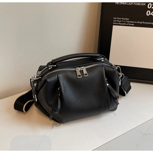 Detail of black pebbled leather Boston bag featuring silver zippers and a wide woven strap