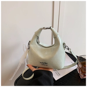 Close-up of mint green shiny leather handbag with white lace bow and pearl charm