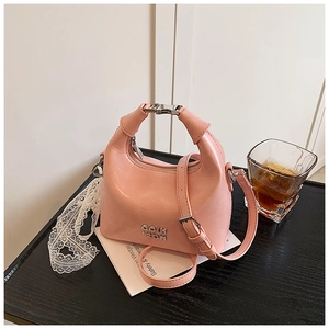 Pink faux leather crossbody bag with metal logo and handle detail on a modern desk
