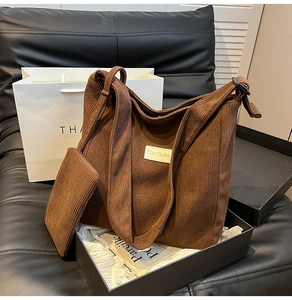 Detailed texture of a brown corduroy tote bag with a matching small zipper pouch on a sofa