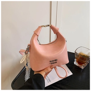 Pink PU leather handbag detail with metal letters and pearl lace charm on wood table