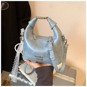 Detail of light blue crescent bag featuring silver hardware and a pearl lace charm