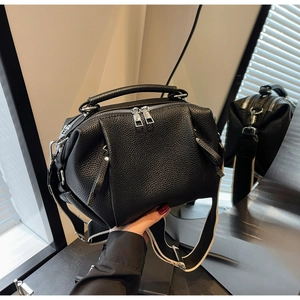 Detail of black lychee grain leather handbag with silver zippers and wide woven strap