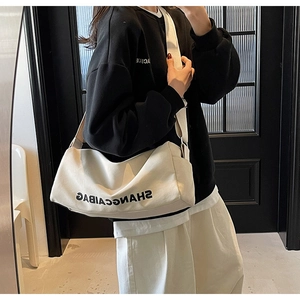 Detail of a large white canvas crossbody bag with black lettering and wide strap