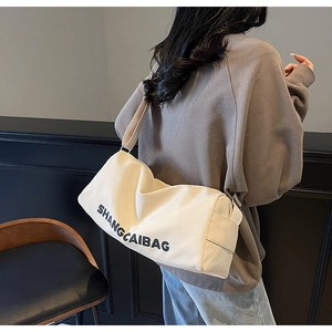 Detail of cream canvas cylinder bag with black SHANGCAIBAG lettering and wide strap