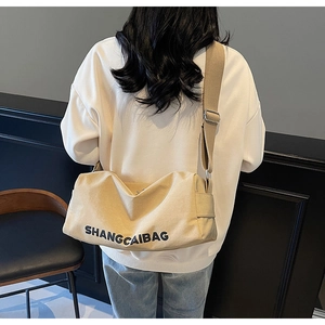 Detail of beige canvas crossbody bag with black lettering and wide adjustable shoulder strap