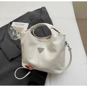 Detail of a creamy white bucket bag with triangular metal accent and soft leather texture
