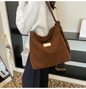 Close-up of deep brown corduroy tote bag featuring a leather patch on soft knit sweater