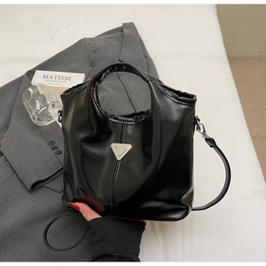 Detailed close-up of glossy black faux leather tote with metallic triangle emblem and texture