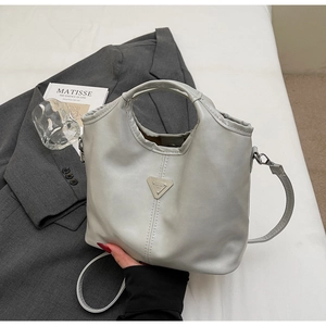 Close-up of light grey bucket bag with triangle metal logo on a grey suit jacket