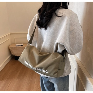 Detail view of khaki canvas cross-body bag featuring a cylindrical Boston shape and white logo