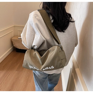 Close-up of olive green canvas shoulder bag with wide strap and white text logo