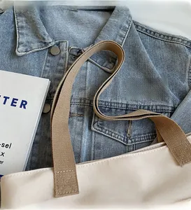 Detail of beige canvas bucket bag featuring a wide brown woven shoulder strap close-up