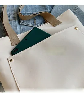 Detail of off-white canvas tote bag featuring front pocket with gold rivet accents