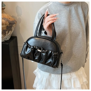 Close-up of black pleated PU leather handbag with top handles and adjustable strap