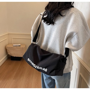 Large black canvas shoulder bag with white lettering shown from the back of a model