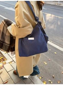 Detailed view of large dark blue corduroy tote bag worn by model in an autumn outdoor setting