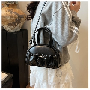 Close-up of a stylish black ruched pillow handbag with metallic buckles and thin strap