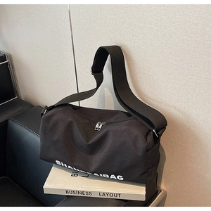 Detailed close-up of a black canvas crossbody bag with white lettering and dual silver zippers
