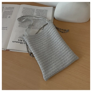 Detail of silver woven crossbody phone bag with metal chain strap on a wooden desk
