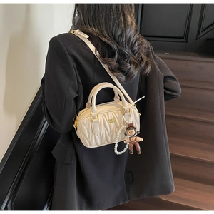 Detalle de bolso acolchado crema con logo dorado, cadena de perlas y colgante muñeca