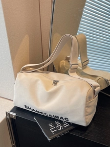 Creamy white canvas barrel bag with adjustable strap and silver zippers for travel