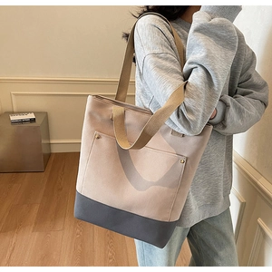 Detail of canvas tote bag showing two-tone stitching and front pocket with metal studs