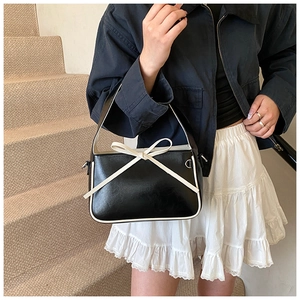 Détail du sac seau noir brillant avec nœud blanc et finitions en cuir contrastées