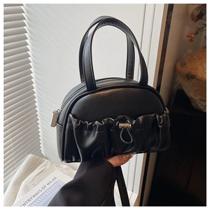 Detail view of black matte leather handbag with unique pleated pocket and metal hardware