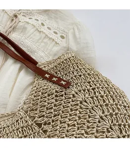 Detail of woven straw tote with hollow-out pattern and leather handles with white stitching
