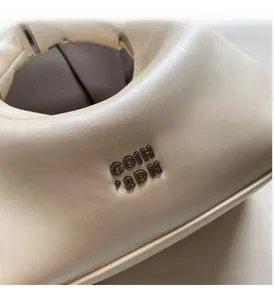 Detail of soft cream faux leather handbag featuring dark grey metallic logo hardware