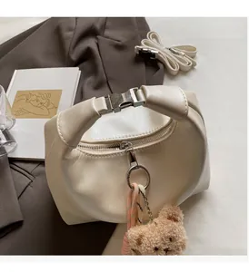 Detail of off-white dumpling bag with silver metal handle and plush bear charm