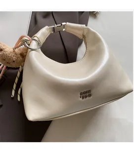Detail of creamy white crescent hobo bag with embossed logo and brown bear charm