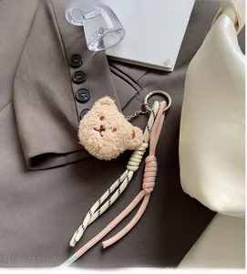 Detail of plush bear charm with woven ropes on a stylish croissant crossbody handbag