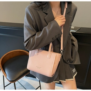 Pink woven bucket bag shown on model with handle and adjustable shoulder strap detail