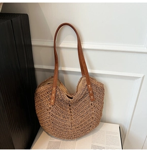 Close-up of handwoven straw tote with brown leather handles and reinforced stitching