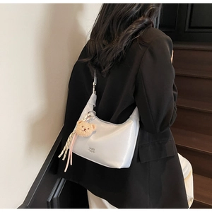 Detail of light blue crescent bag with plush bear charm and ribbon on black blazer