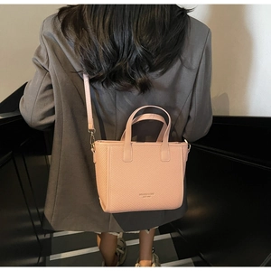 Pink woven texture crossbody bag with shoulder strap shown on a gray blazer backdrop