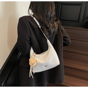 Detailed view of light gray moon-shaped bag with plush bear charm worn by a model
