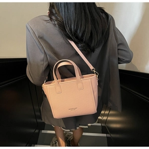 Detail of pink woven leather bucket bag featuring a shoulder strap on a grey suit model