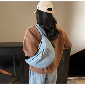 Detail of light blue crescent dumpling bag with wide strap on model in indoor setting