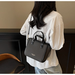 Detail view of black woven tote bag featuring gold hardware and logo print on model