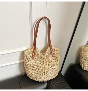 Detail of hollow woven straw tote bag featuring brown leather straps and cross stitching