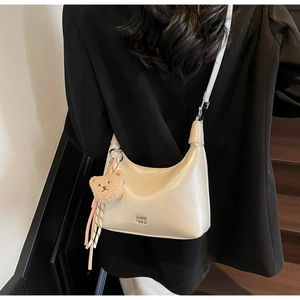 Off-white matte leather dumpling bag with brown teddy bear charm on black blazer