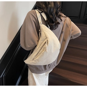 Detail of a beige half-moon crossbody bag showing nylon fabric and braided zipper pull