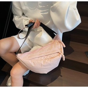 Detail of pink nylon dumpling bag with adjustable wide strap shown on wooden stairs
