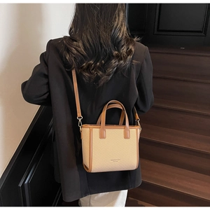 Close-up of minimalist beige woven bucket bag with brown leather handles and strap
