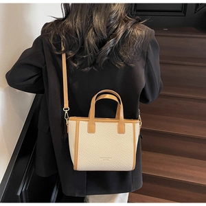 Detail of cream woven bucket bag with brown leather trim worn by model on a staircase