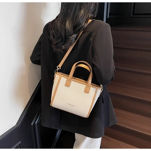 Detail of beige woven bucket bag with brown leather trim held by a model on stairs