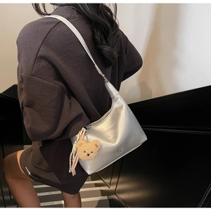 Silver metallic dumpling bag with plush bear charm worn by a model on a staircase